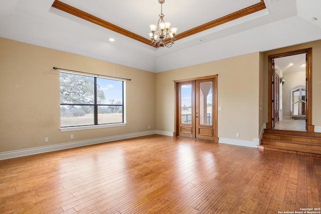 empty room with ornamental molding, light hardwood / wood-style flooring, a notable chandelier, and a raised ceiling