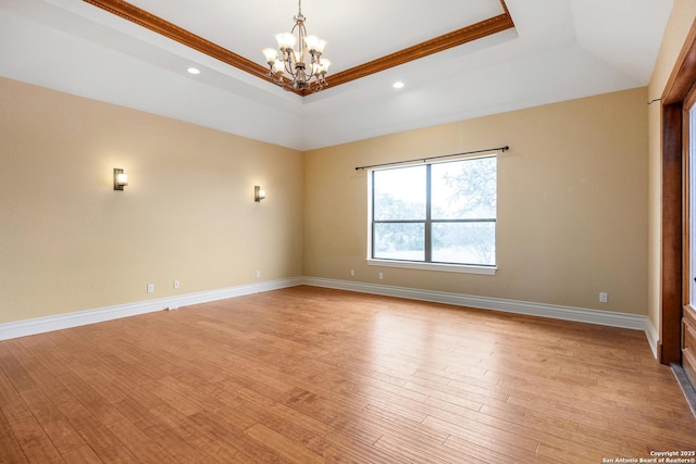 unfurnished room with light hardwood / wood-style floors, a tray ceiling, ornamental molding, and an inviting chandelier