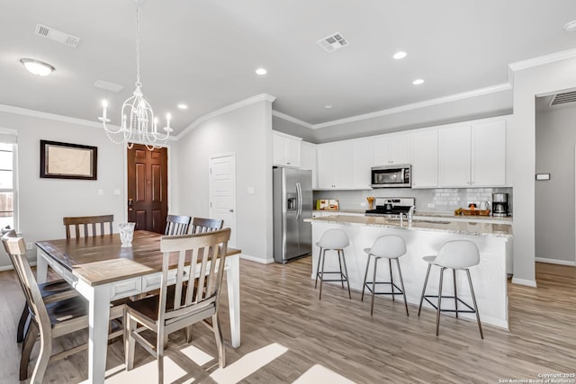 dining room with sink, light hardwood / wood-style floors, a chandelier, and ornamental molding