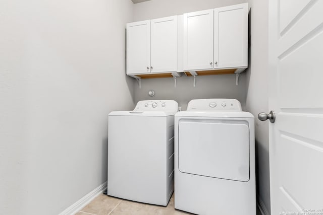 clothes washing area featuring separate washer and dryer, light tile patterned floors, and cabinets