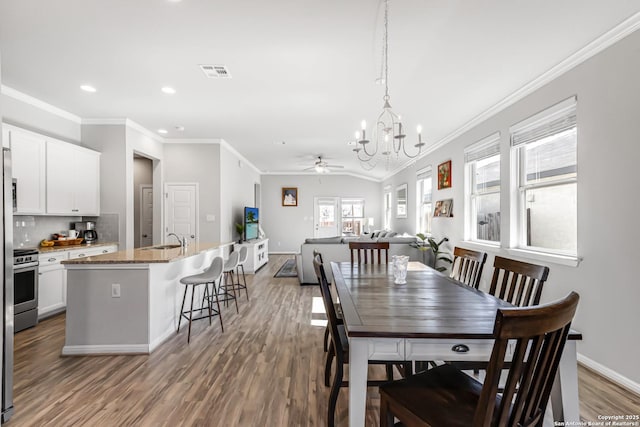 dining space featuring hardwood / wood-style flooring, ceiling fan with notable chandelier, ornamental molding, and vaulted ceiling