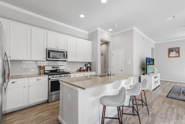 kitchen featuring white cabinets, stainless steel appliances, an island with sink, sink, and light stone counters