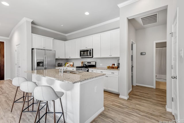 kitchen with sink, white cabinets, light stone counters, an island with sink, and stainless steel appliances