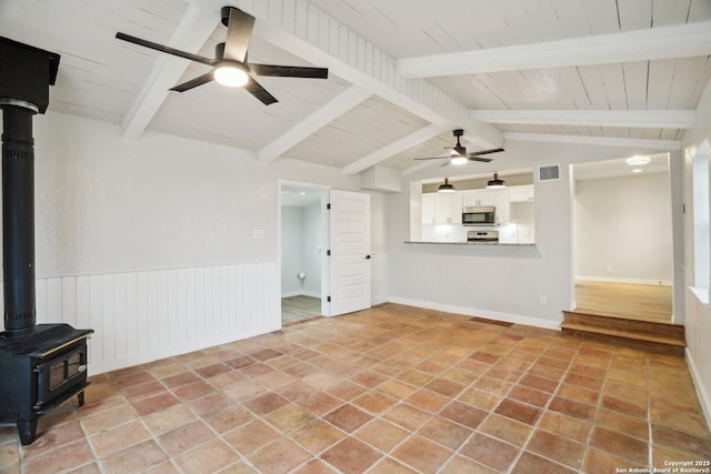 unfurnished living room with ceiling fan, a wood stove, lofted ceiling with beams, and wooden ceiling