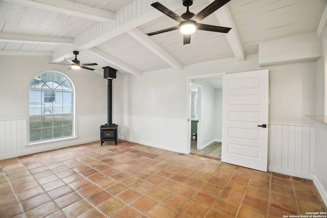 unfurnished living room with ceiling fan, a wood stove, tile patterned floors, and lofted ceiling with beams