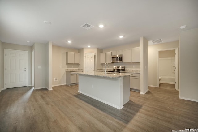 kitchen featuring a center island with sink, hardwood / wood-style flooring, light stone countertops, and stainless steel appliances