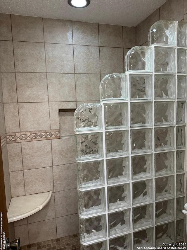 bathroom with tiled shower and a textured ceiling