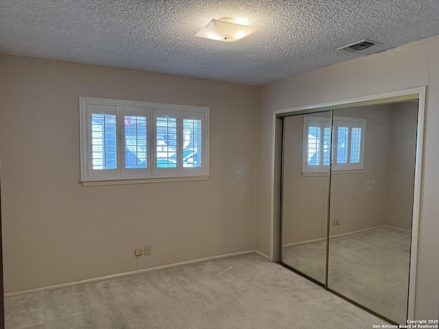 unfurnished bedroom featuring light colored carpet, a textured ceiling, a closet, and multiple windows