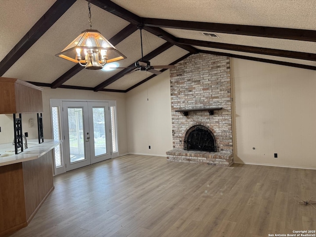 unfurnished living room with a fireplace, light wood-type flooring, french doors, and vaulted ceiling with beams