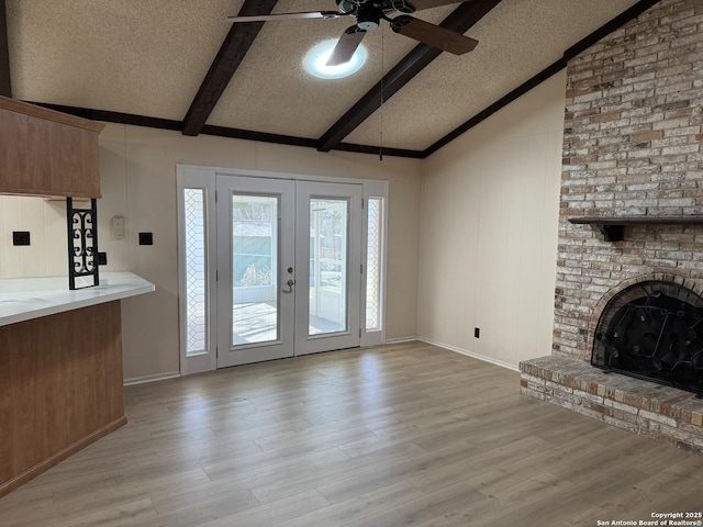 unfurnished living room with a textured ceiling, french doors, a fireplace, lofted ceiling with beams, and light wood-type flooring