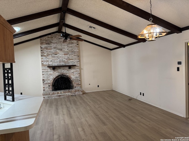 unfurnished living room with hardwood / wood-style floors, a textured ceiling, a brick fireplace, ceiling fan with notable chandelier, and lofted ceiling with beams