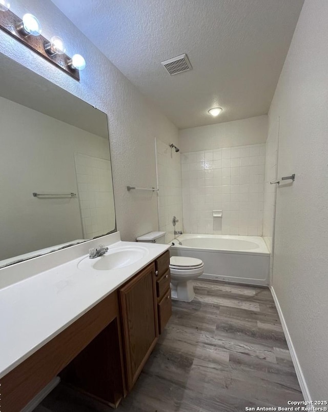 full bathroom with a textured ceiling, hardwood / wood-style floors, tiled shower / bath, vanity, and toilet