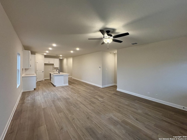 unfurnished living room featuring sink, wood-type flooring, and ceiling fan