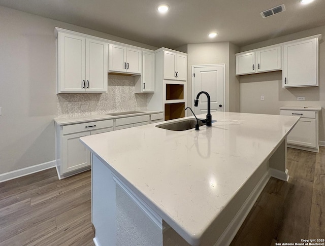 kitchen featuring sink, white cabinets, tasteful backsplash, hardwood / wood-style flooring, and an island with sink