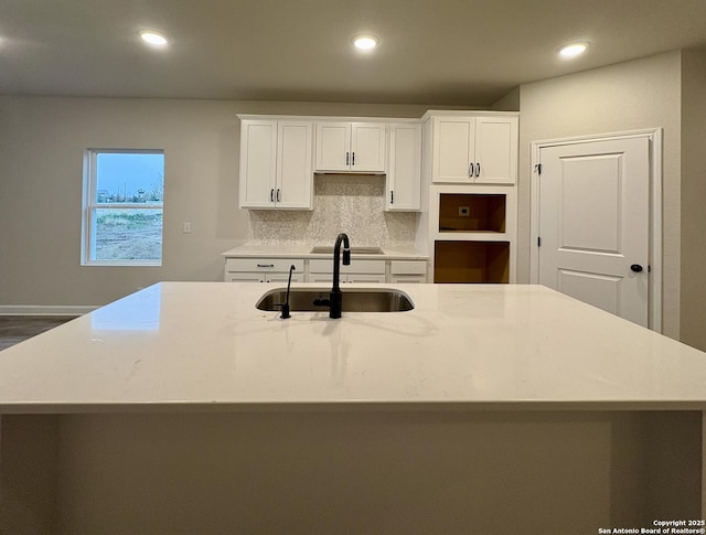 kitchen featuring white cabinetry, sink, decorative backsplash, and a large island with sink