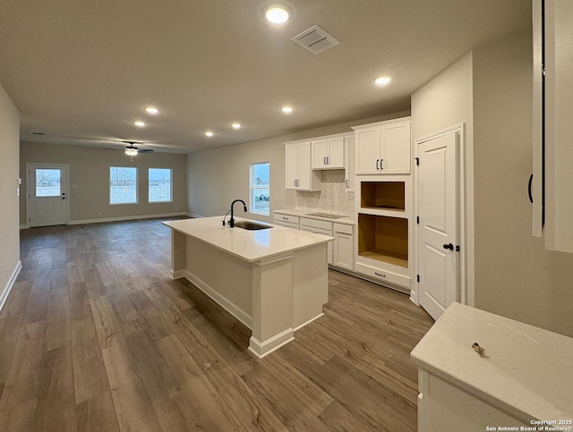 kitchen featuring decorative backsplash, black electric cooktop, sink, white cabinets, and an island with sink