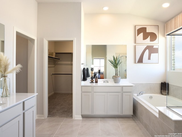 bathroom with tiled bath, tile patterned floors, lofted ceiling, and vanity