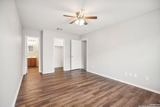 unfurnished bedroom featuring ensuite bathroom, ceiling fan, dark hardwood / wood-style flooring, a spacious closet, and a closet