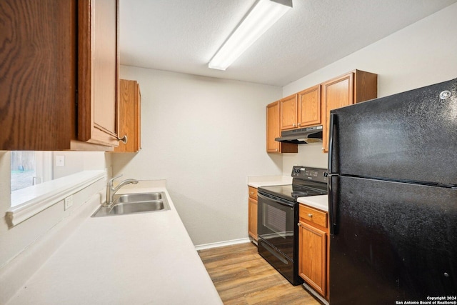 kitchen featuring sink, black appliances, a textured ceiling, and light wood-type flooring