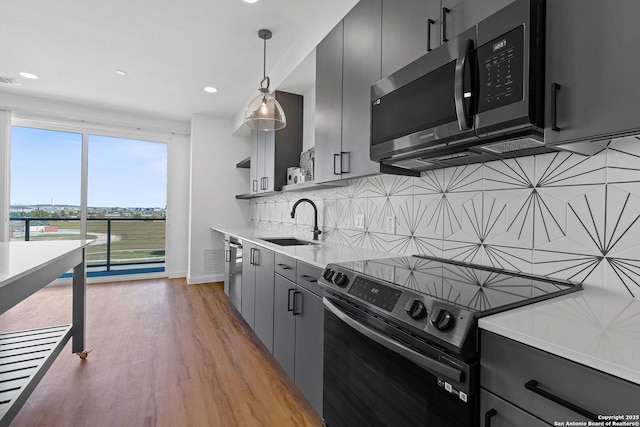 kitchen featuring sink, light wood-type flooring, pendant lighting, backsplash, and range with electric stovetop