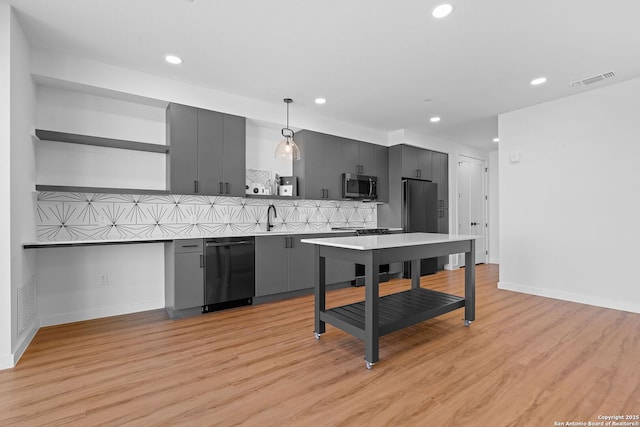 kitchen with pendant lighting, black appliances, tasteful backsplash, sink, and light hardwood / wood-style flooring