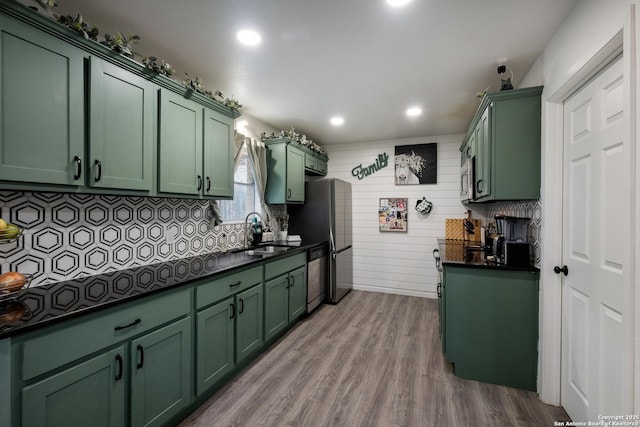 kitchen with sink, green cabinetry, light hardwood / wood-style floors, decorative backsplash, and stainless steel appliances