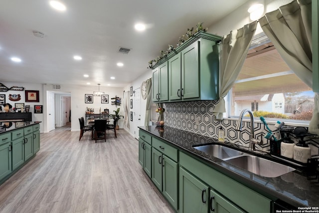 kitchen featuring hanging light fixtures, green cabinetry, sink, light hardwood / wood-style flooring, and backsplash