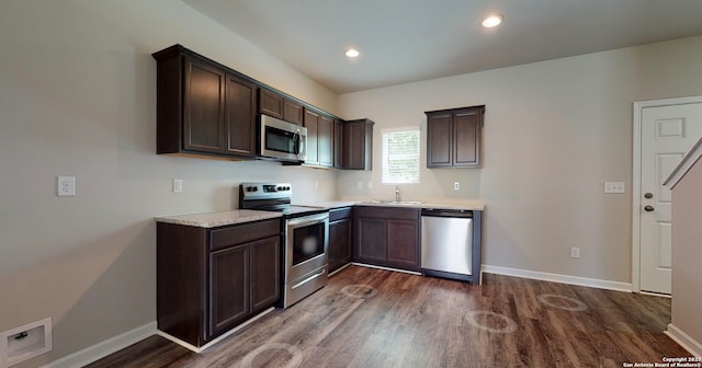 kitchen featuring dark hardwood / wood-style flooring, sink, stainless steel appliances, light stone countertops, and dark brown cabinetry