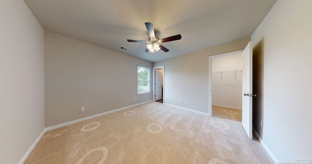 unfurnished bedroom featuring a closet, ceiling fan, a spacious closet, and light colored carpet