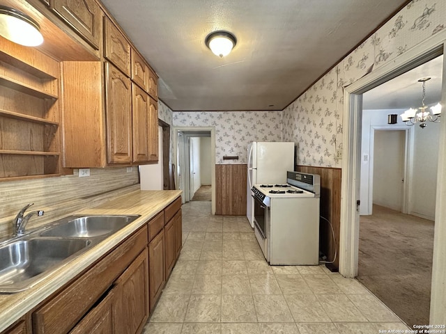 kitchen featuring light carpet, hanging light fixtures, white range with gas stovetop, sink, and a notable chandelier