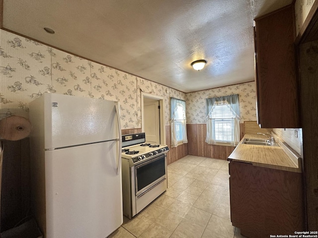 kitchen with wood walls, sink, white appliances, and a textured ceiling