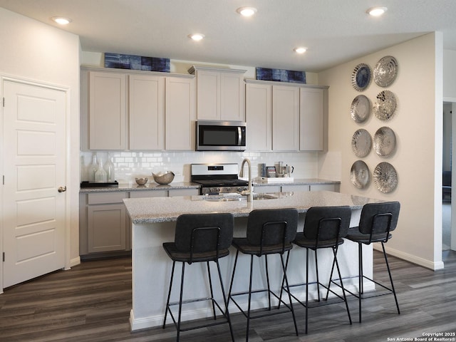 kitchen featuring decorative backsplash, appliances with stainless steel finishes, dark hardwood / wood-style flooring, and an island with sink