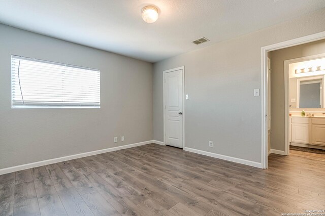 unfurnished bedroom with connected bathroom and hardwood / wood-style floors