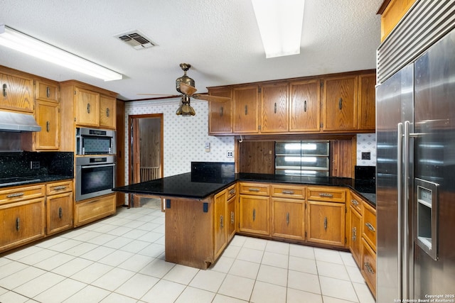 kitchen featuring a textured ceiling, appliances with stainless steel finishes, kitchen peninsula, ceiling fan, and backsplash