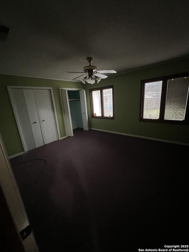 unfurnished bedroom featuring multiple closets, carpet floors, and ceiling fan