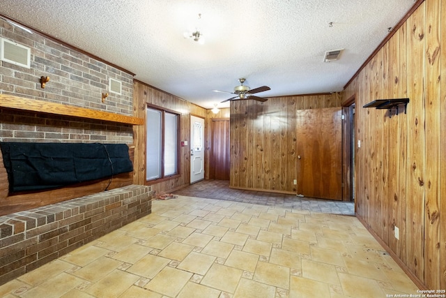 unfurnished living room with ceiling fan, ornamental molding, wooden walls, and a textured ceiling