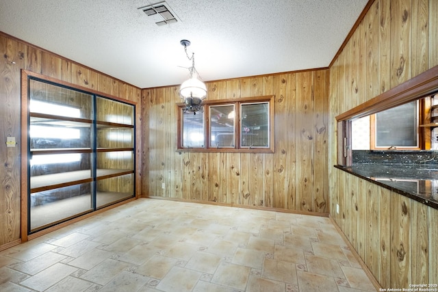 unfurnished dining area featuring ornamental molding, a textured ceiling, and wood walls