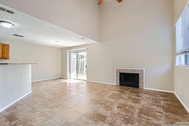 unfurnished living room with a tile fireplace, a textured ceiling, a high ceiling, and ceiling fan