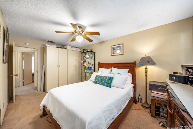 bedroom featuring ceiling fan, light colored carpet, and a textured ceiling