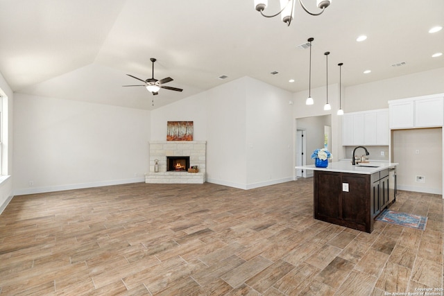 kitchen featuring a fireplace, sink, dark brown cabinets, pendant lighting, and an island with sink