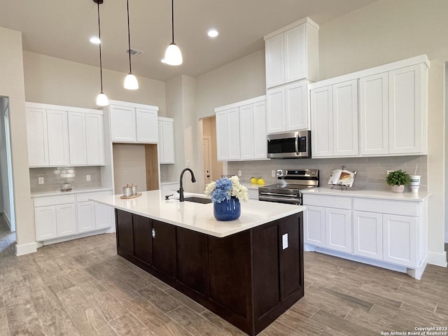 kitchen with decorative light fixtures, white cabinetry, appliances with stainless steel finishes, and an island with sink