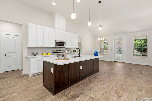 kitchen with an island with sink, vaulted ceiling, hanging light fixtures, and appliances with stainless steel finishes