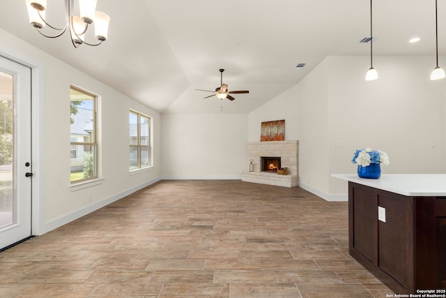 unfurnished living room featuring a fireplace, ceiling fan with notable chandelier, and vaulted ceiling