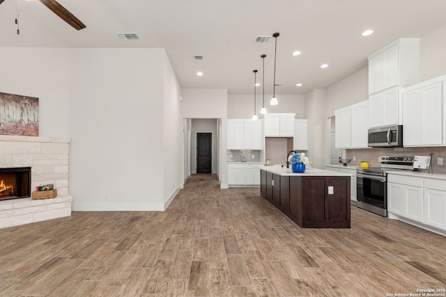 kitchen featuring backsplash, hanging light fixtures, appliances with stainless steel finishes, and an island with sink