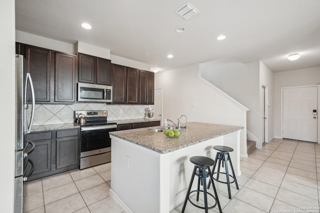 kitchen with appliances with stainless steel finishes, tasteful backsplash, light tile patterned floors, a breakfast bar, and a center island with sink