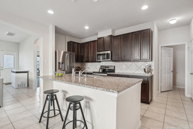 kitchen with appliances with stainless steel finishes, sink, light stone counters, a breakfast bar, and an island with sink