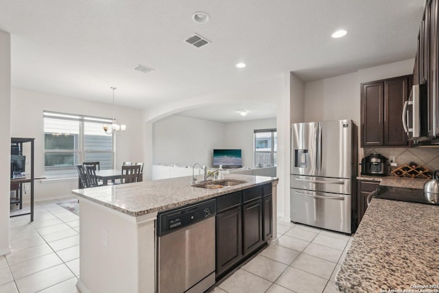 kitchen with light stone countertops, sink, dark brown cabinets, stainless steel appliances, and a center island with sink