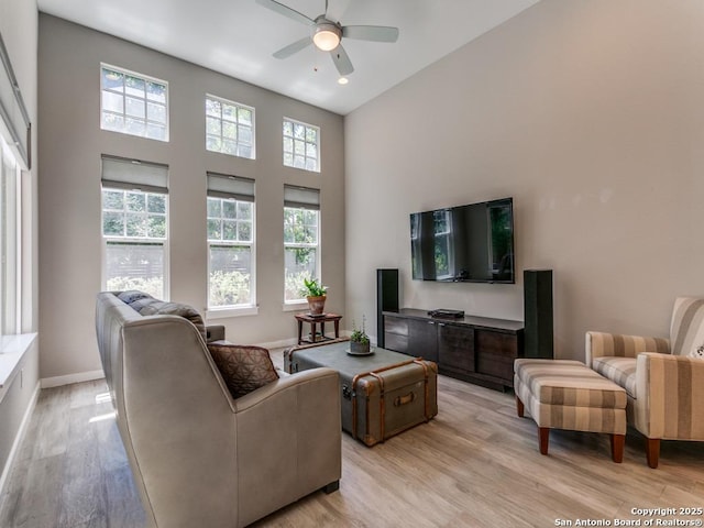 living room featuring ceiling fan, light hardwood / wood-style flooring, and a towering ceiling