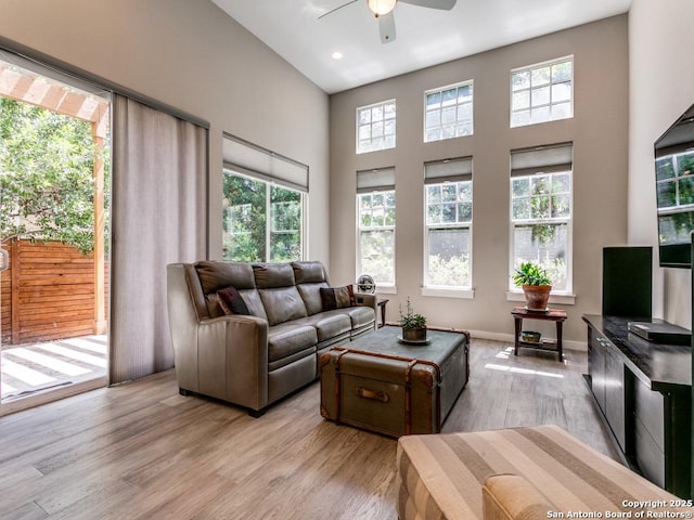 living room with light wood-type flooring, a high ceiling, and ceiling fan