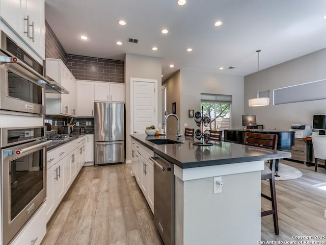 kitchen with a kitchen island with sink, white cabinets, sink, decorative light fixtures, and stainless steel appliances